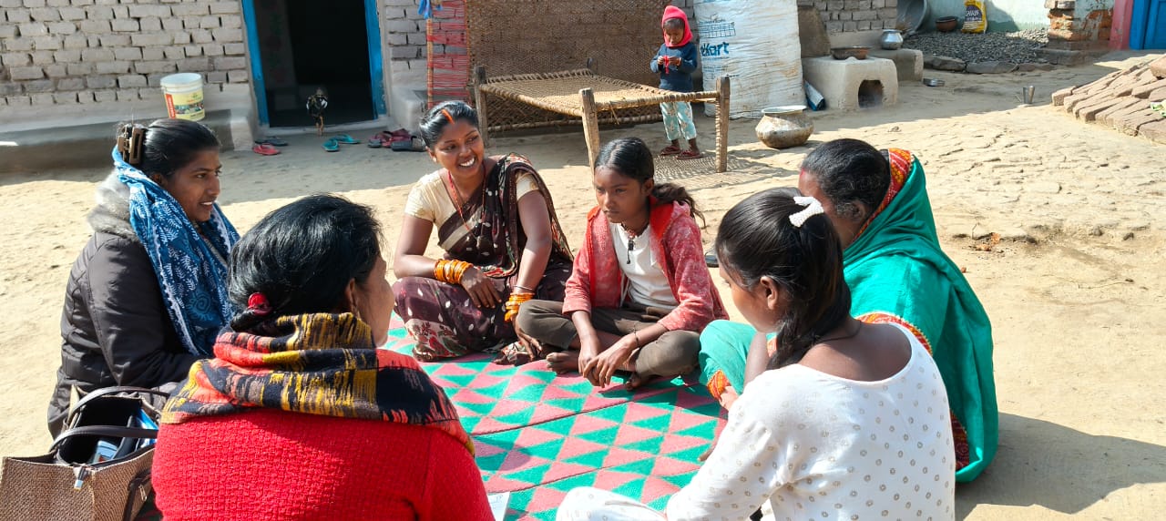 Community engagement for women's empowerment "Women and girls sitting outdoors discussing social issues.