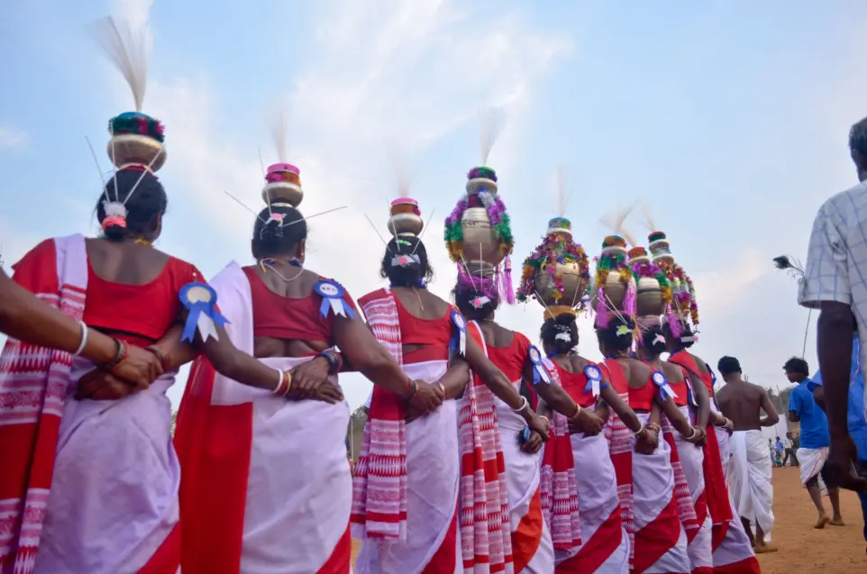 Tribal Dance Performance with Live Drumming at a Festiva Tribal women in green and red sarees dancing in a line, accompanied by drummers in yellow jerseys at a cultural festival.