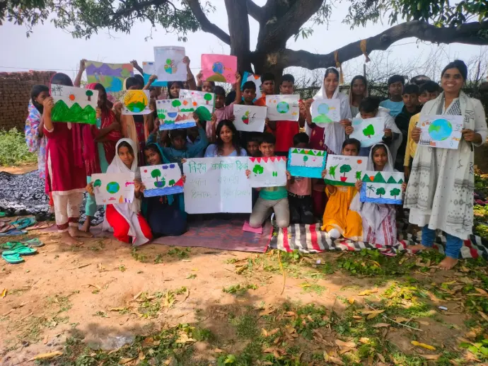 Environmental Awareness Event with Children A group of children and young adults holding colorful drawings of trees, the Earth, and nature, celebrating environmental awareness under a large tree.