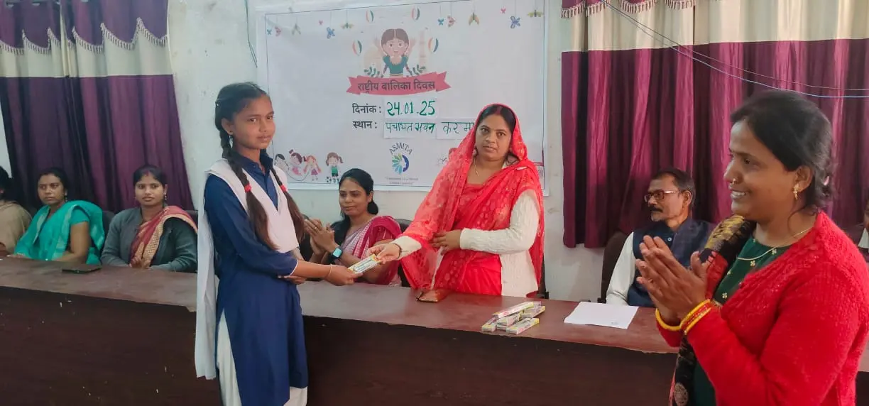 A young girl receiving an award from a woman during a National Girl Child Day event at a community gathering.